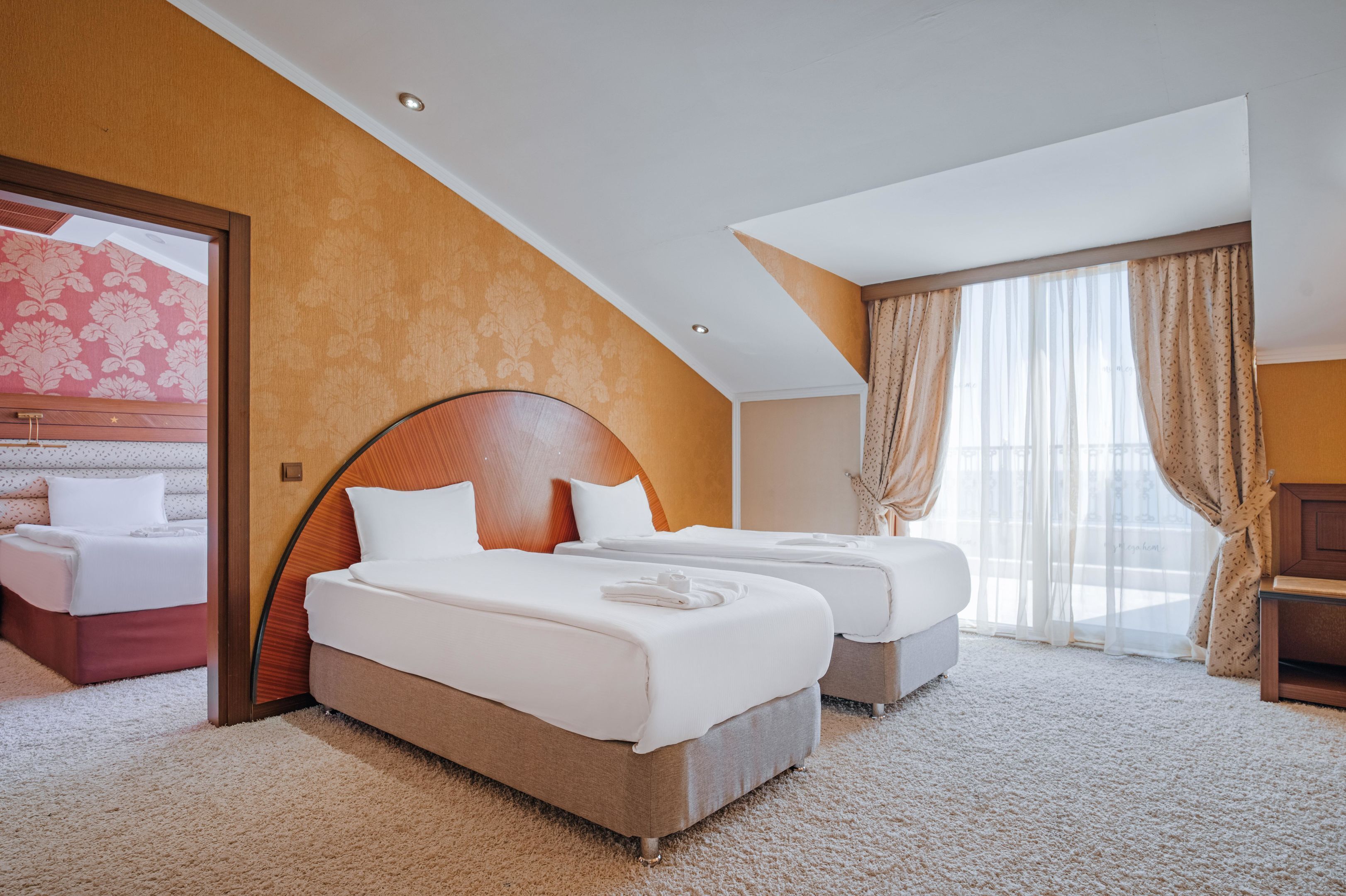 A hotel room with two beds, a large window with sheer curtains, and a wooden headboard.