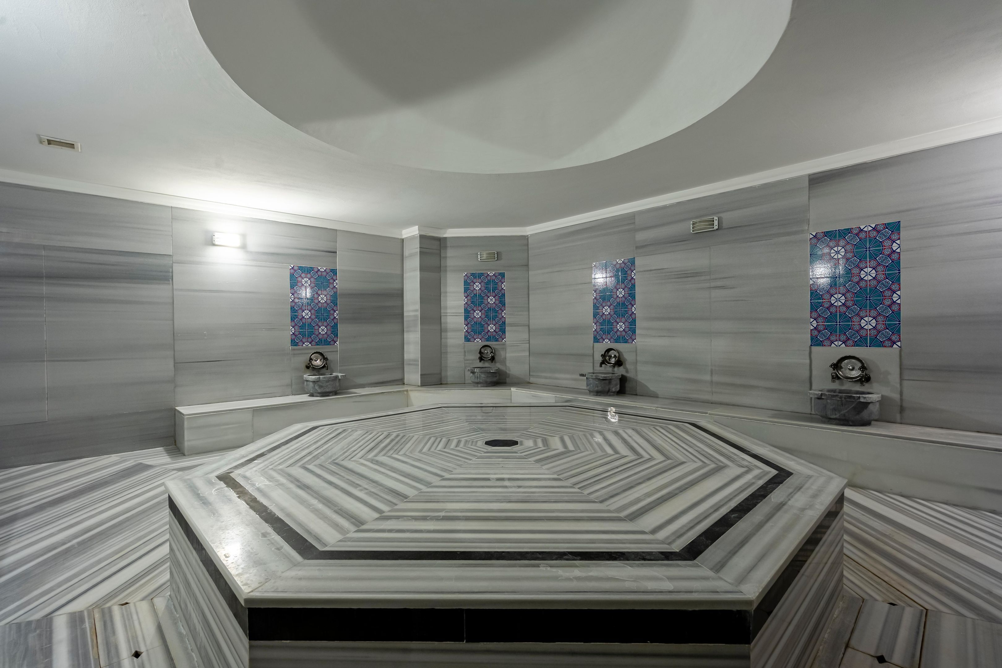 A modern bathroom with a central circular sink, marble flooring, and decorative tile walls.