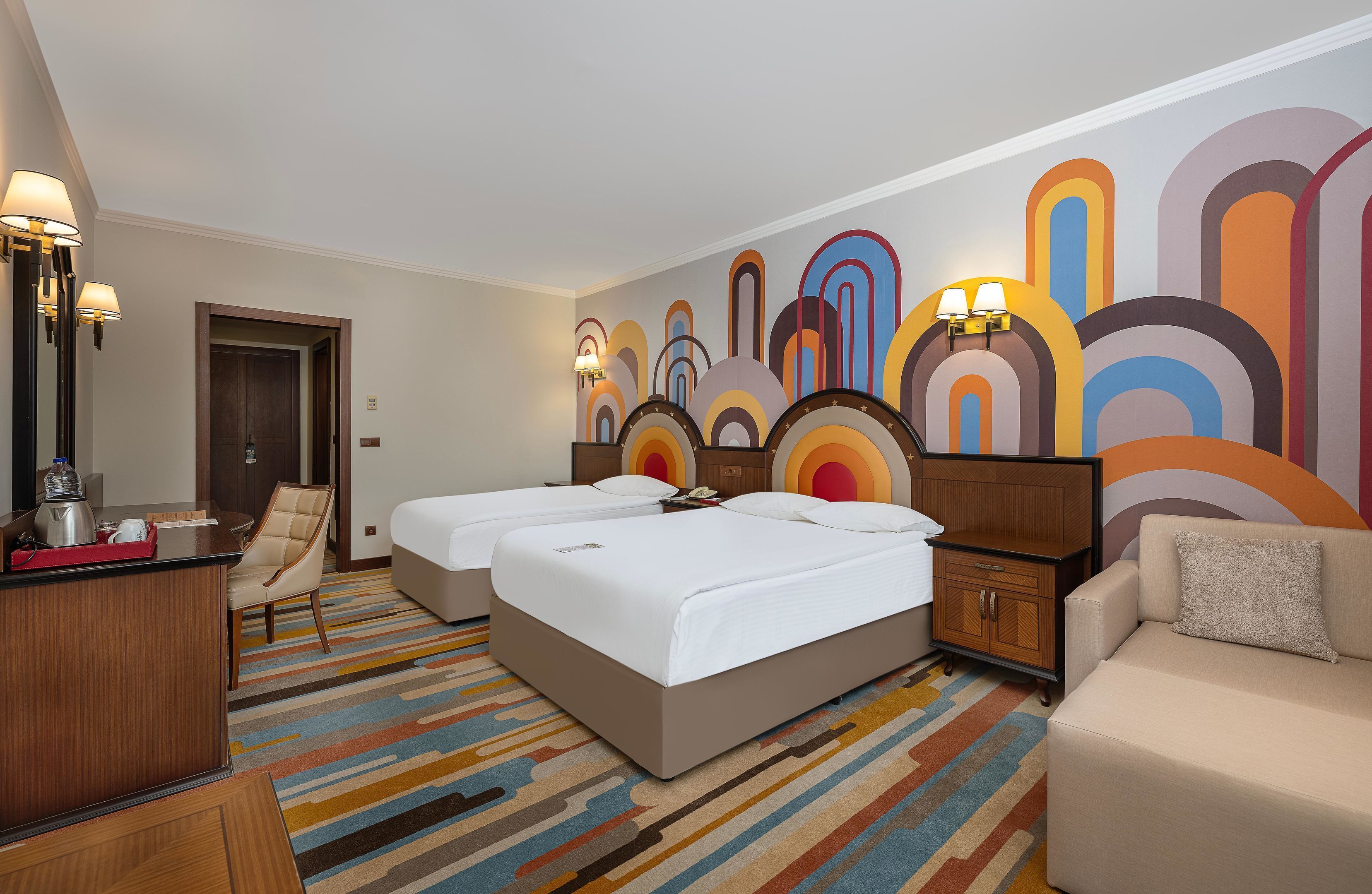 A hotel room with two beds, a desk, a chair, and a sofa.