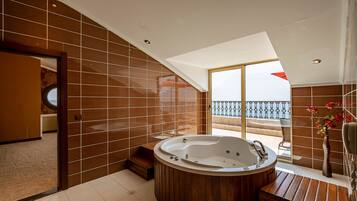 A modern bathroom with a freestanding bathtub, wooden flooring, and a large window offering a view of the balcony.