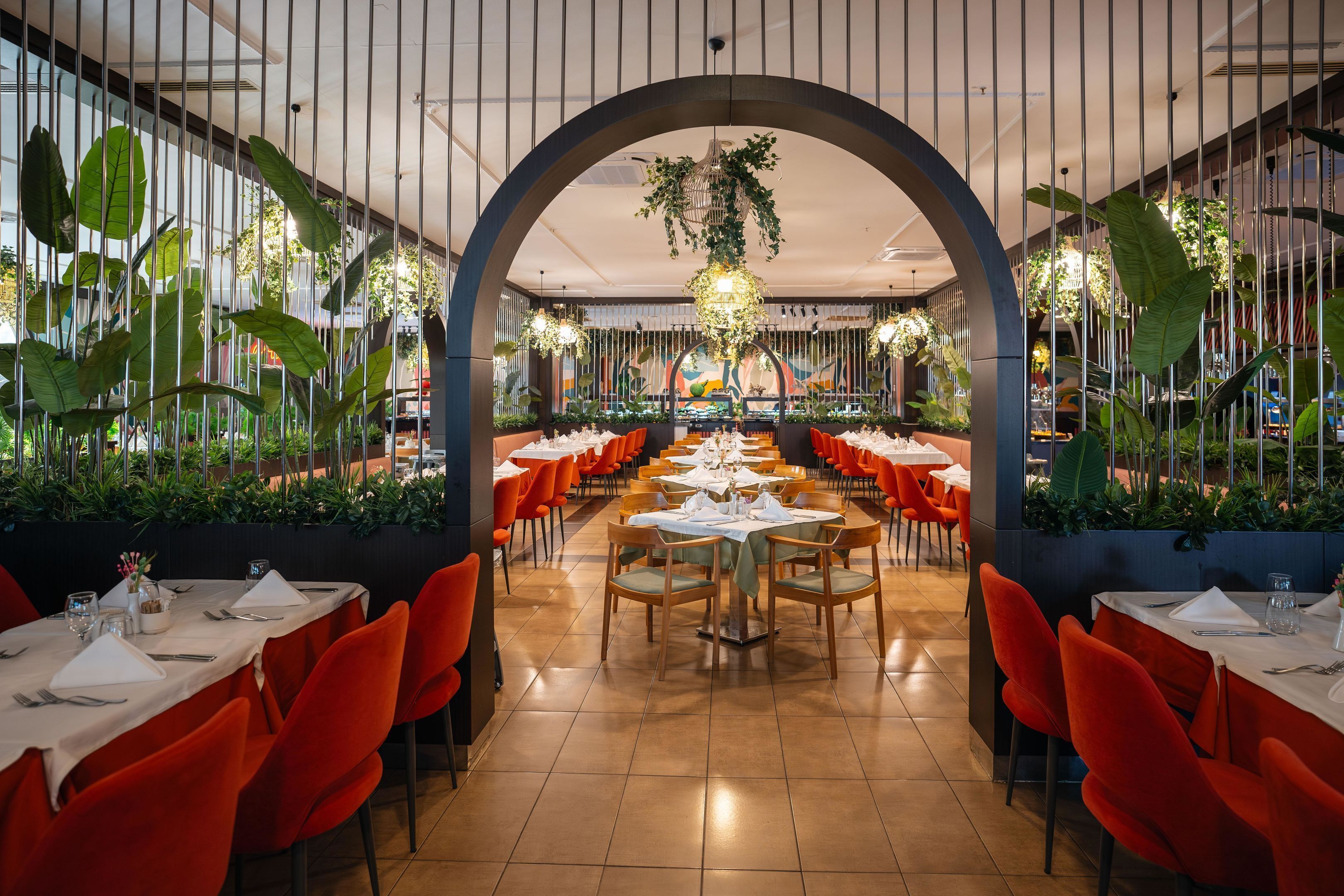 A restaurant with a long dining area, red chairs, and tables set with white tablecloths.