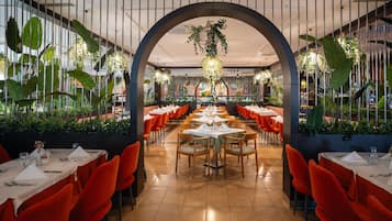 Un restaurante con un amplio salón comedor, sillas rojas y mesas dispuestas con manteles blancos.