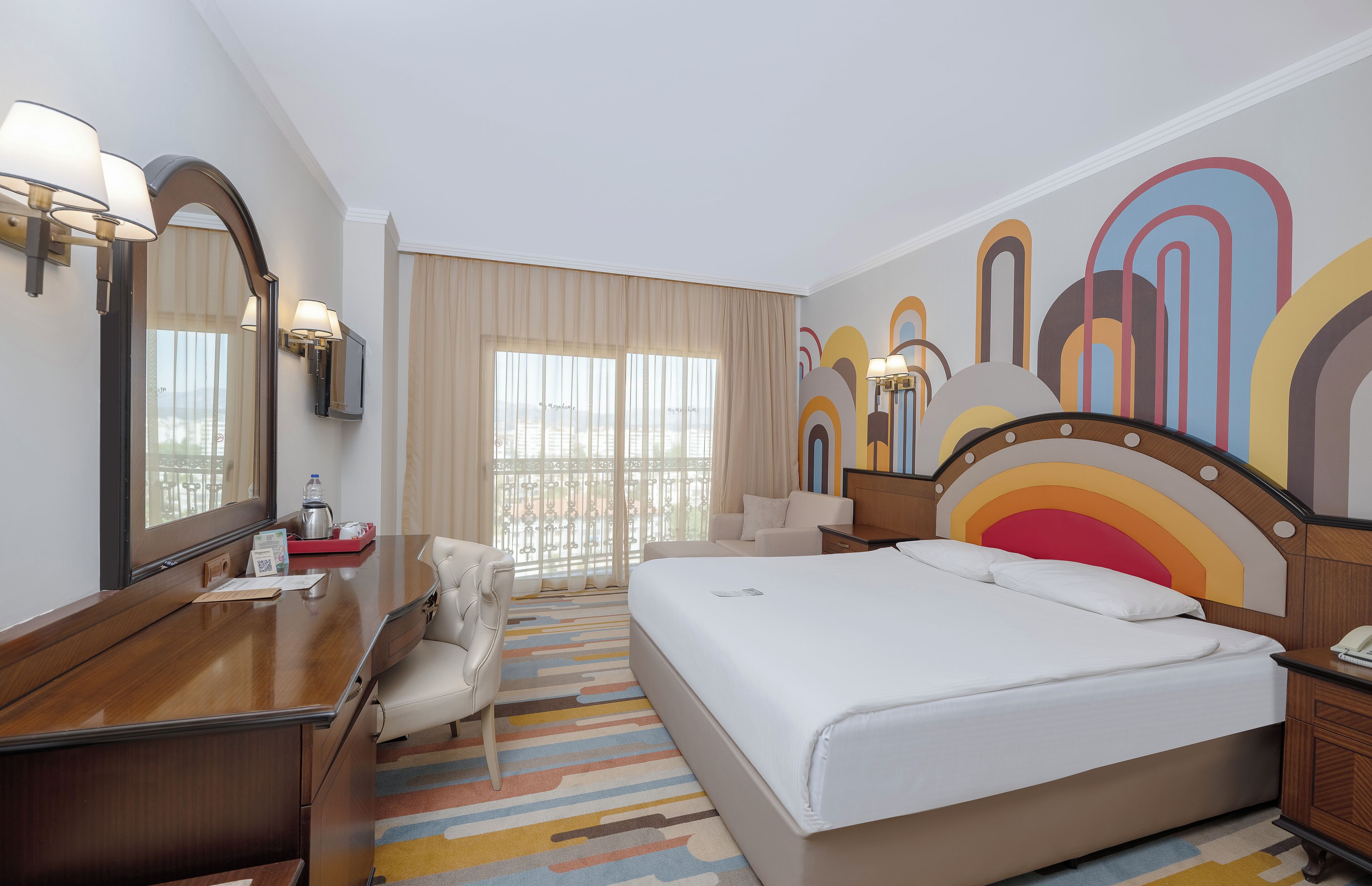 Habitación de hotel con una cama grande, un escritorio con silla, un espejo y un diseño de pared colorido.