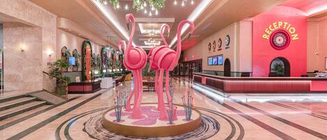 A hotel lobby with a reception desk, a large decorative flamingo sculpture, and a circular seating area.