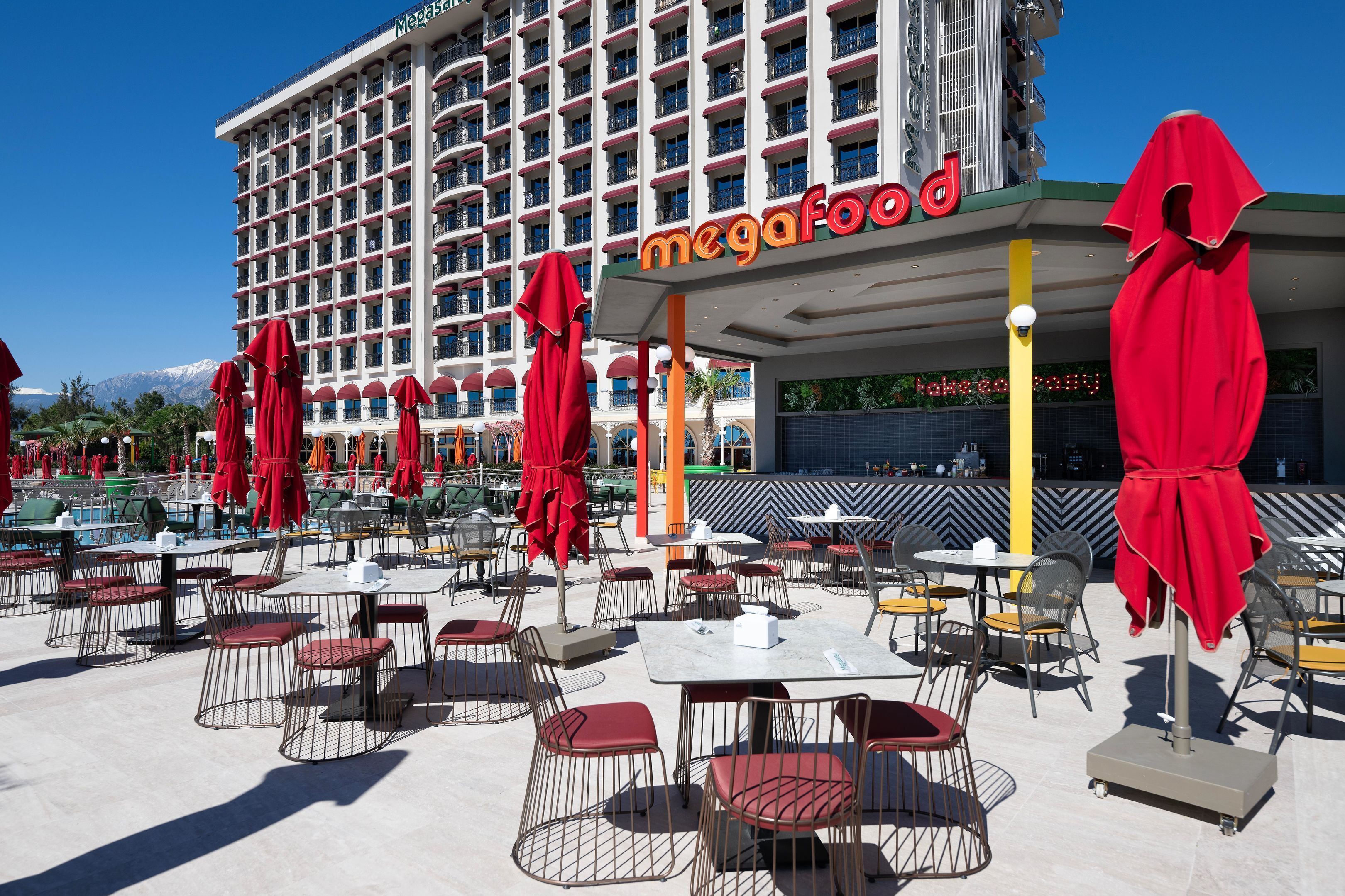 Un hotel con área de comedor al aire libre, sombrillas rojas y un cartel que dice "megafood".