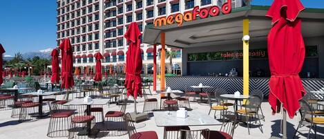 Un hotel con área de comedor al aire libre, sombrillas rojas y un cartel que dice "megafood".