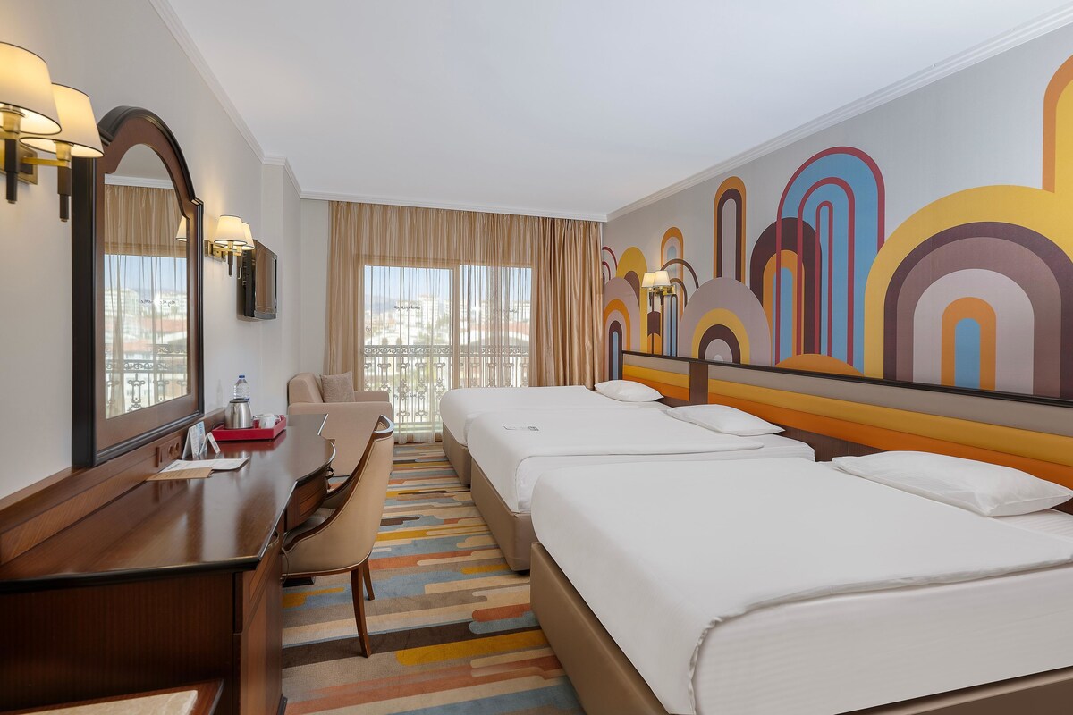 A hotel room with a large bed, a desk with a chair, a TV, and a window with curtains.