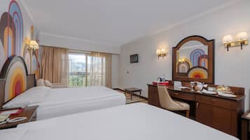 Habitación de hotel con dos camas, un escritorio con silla, una mesita pequeña y un espejo grande.