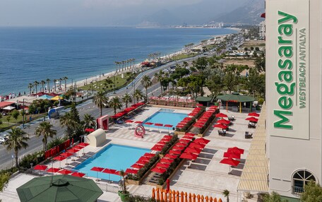 A hotel with a pool area, red umbrellas, and a view of the beach and ocean.