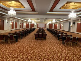 A conference room with rows of tables and chairs, a patterned carpet, and chandeliers.