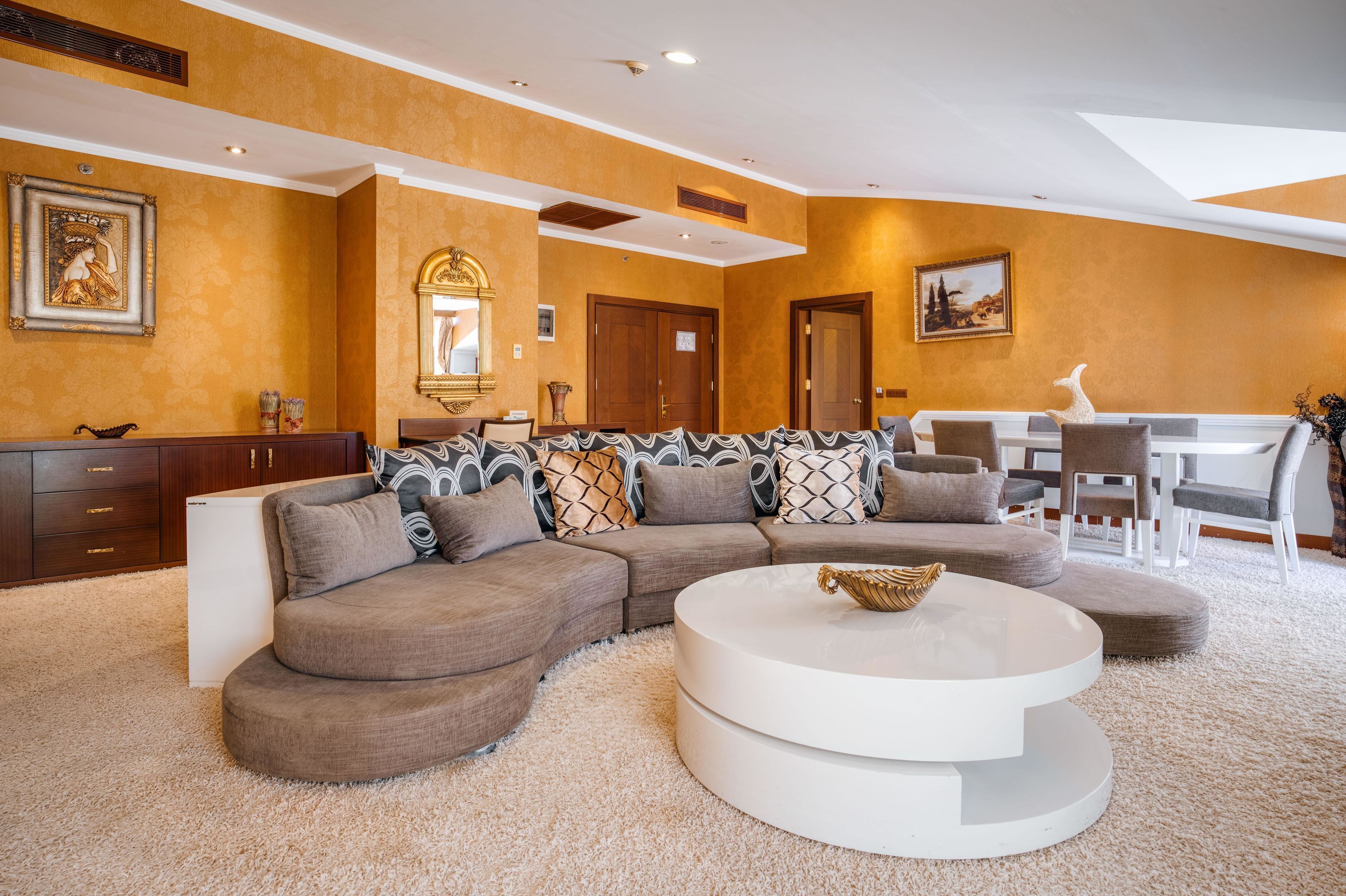 A modern living room with a large sectional sofa, a white coffee table, and a dining area with a white table and chairs.