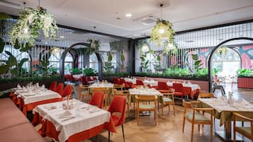 Een restaurant met meerdere tafels voor het dineren, met rode stoelen en witte tafelkleden.