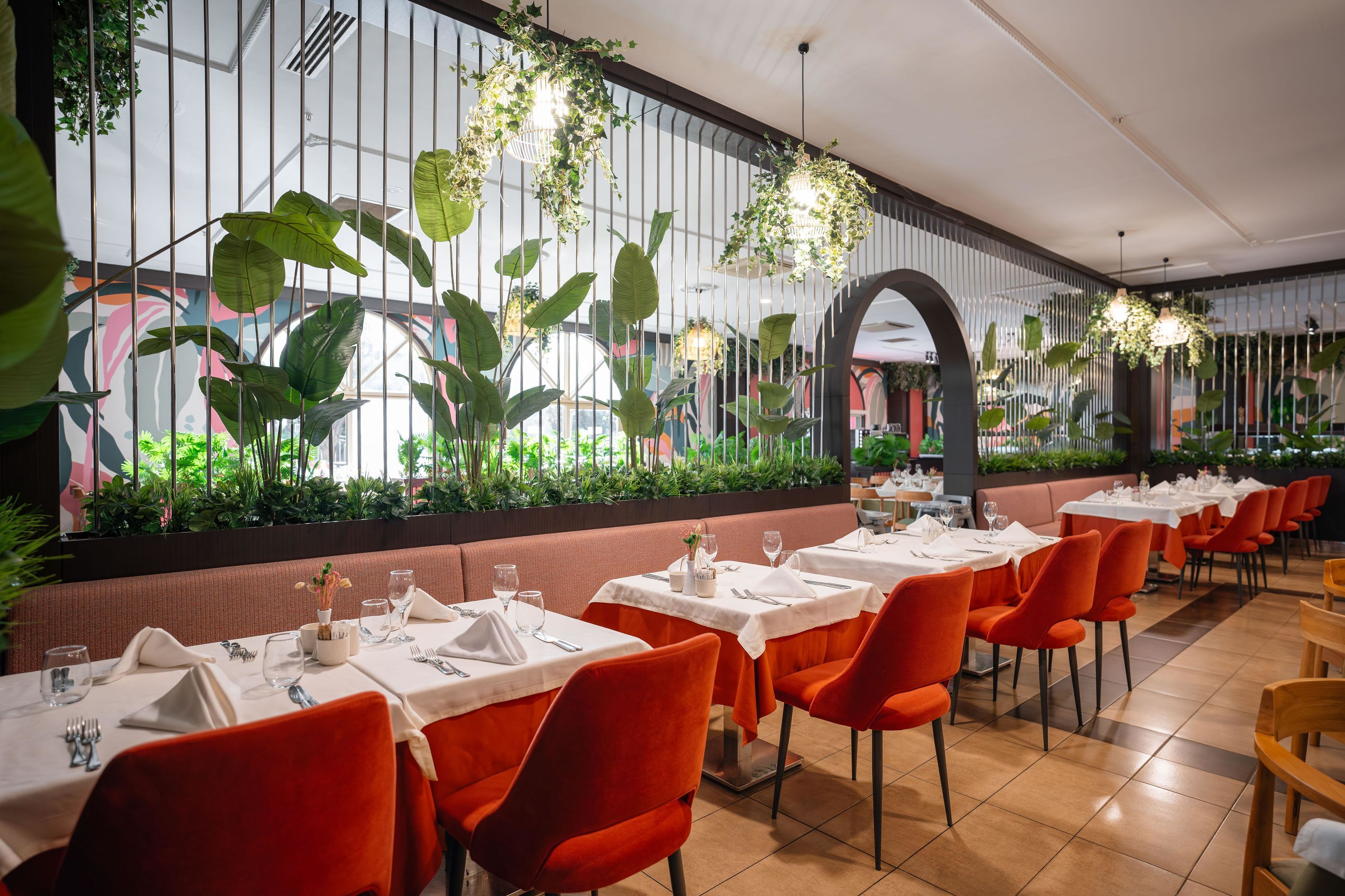 A restaurant with tables set for dining, featuring red chairs and white tablecloths.