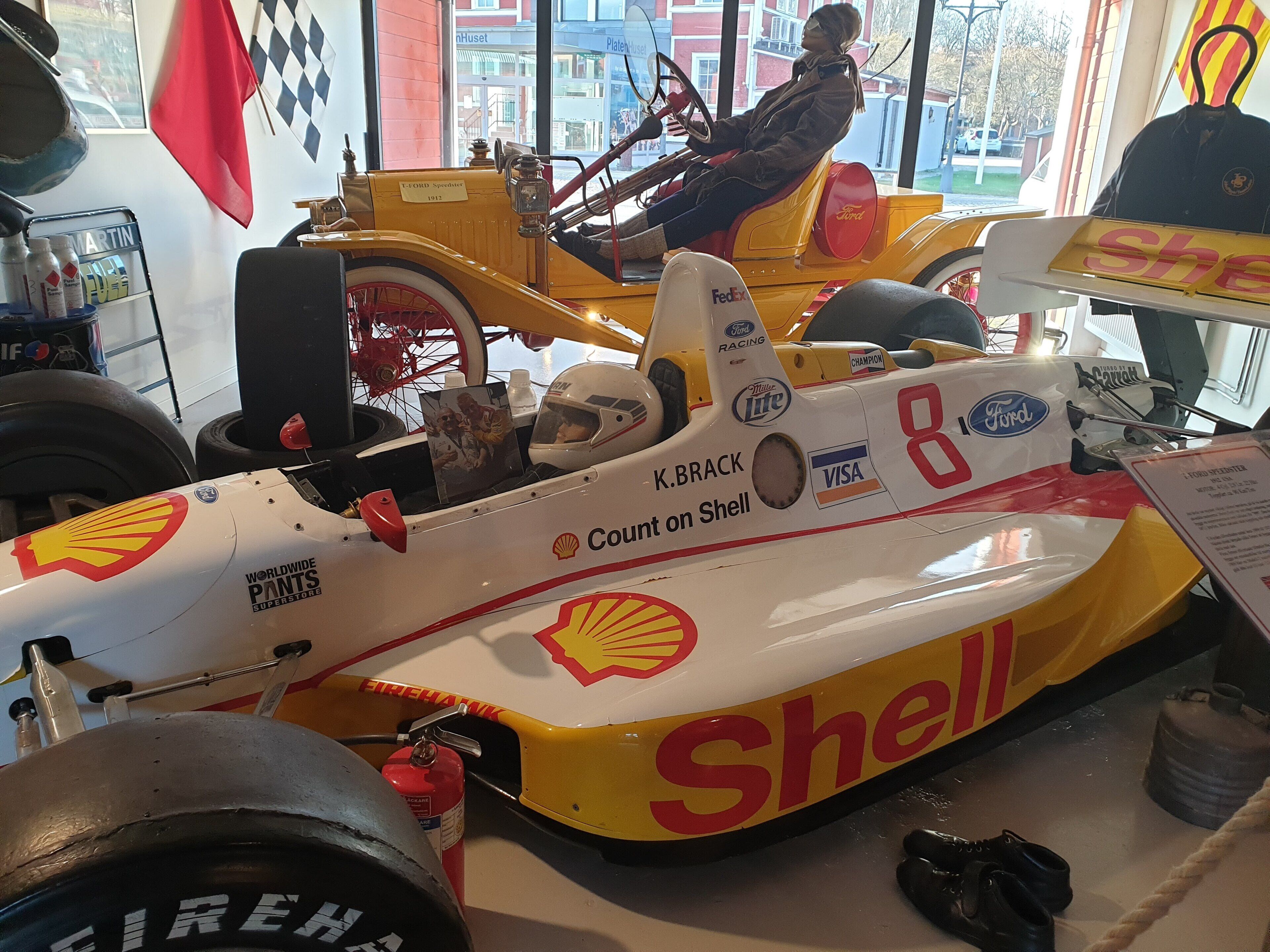 A vintage racing car with the number 8, adorned with sponsor logos like Shell and K. Brack.