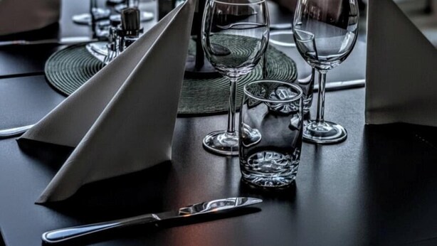 Una mesa lista para comer con una vela, vasos y vista al agua.