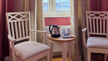 Two white chairs with a table between them, a window with curtains, and a view of a bridge.