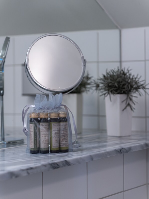 Un lavamanos de baño con un espejo redondo, una planta en maceta y tres botellas de crema corporal.