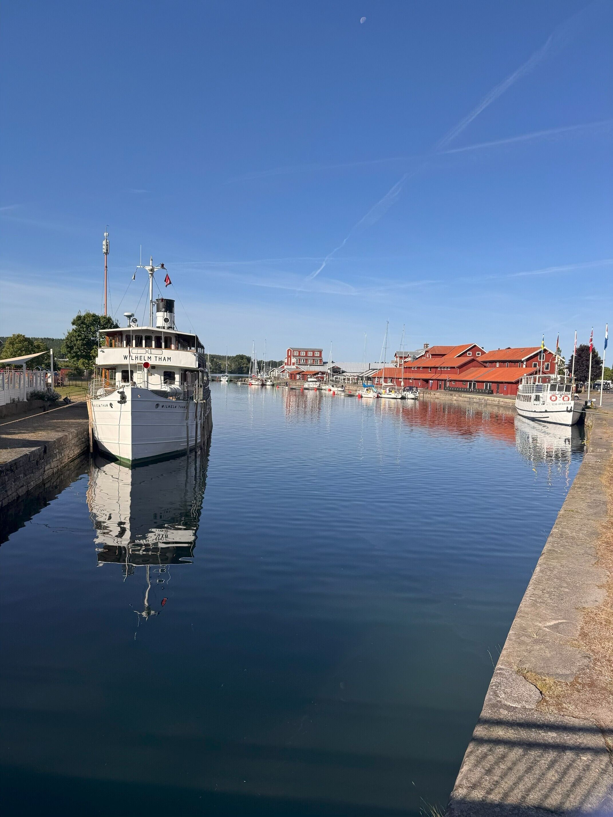 Een rustig water met een boot aan de linkerkant, een steiger aan de rechterkant, en gebouwen op de achtergrond.