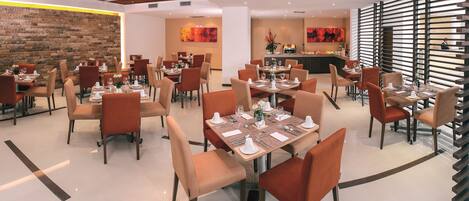 A modern dining area with multiple tables and chairs, a brick accent wall, and a central bar area.