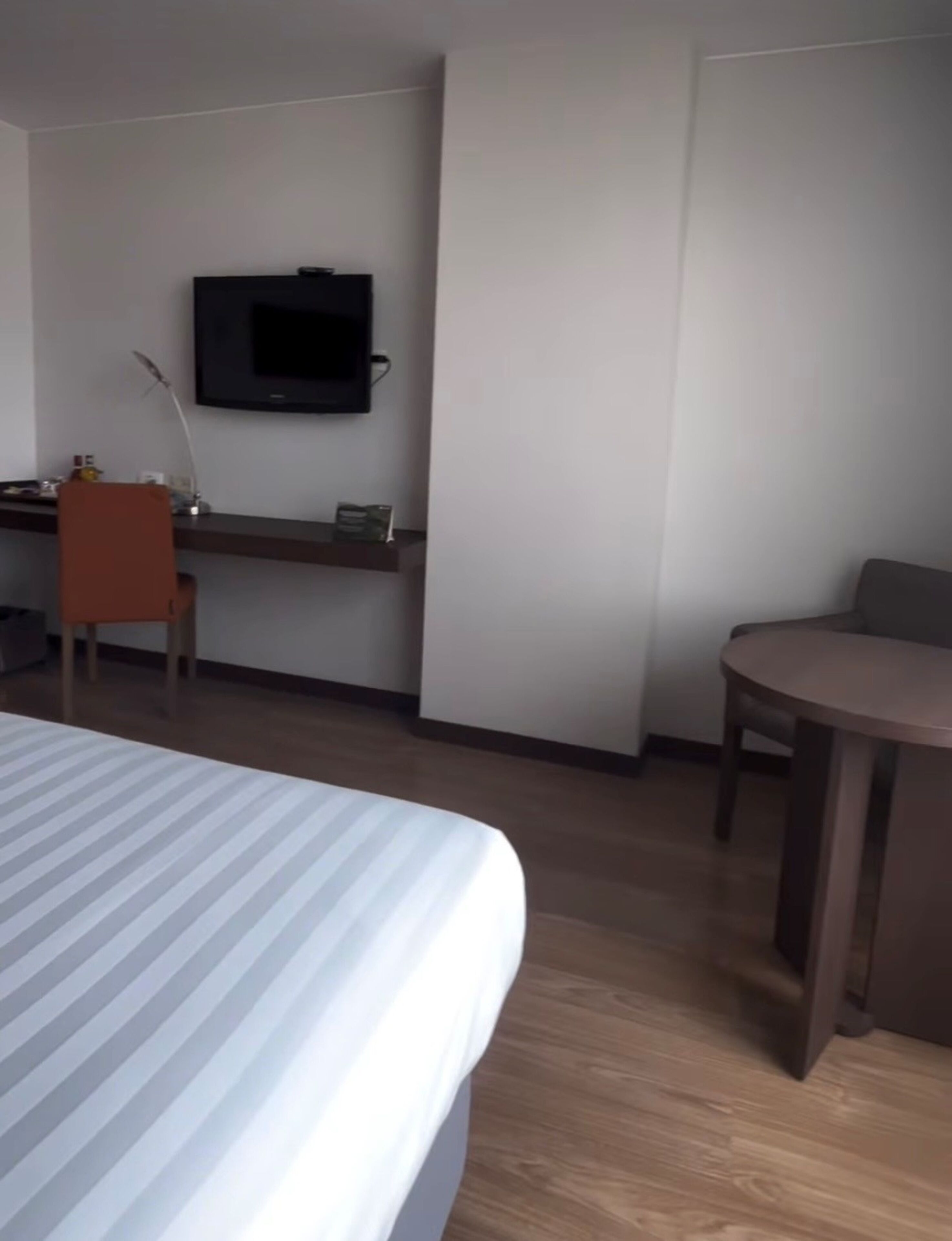 Habitación de hotel con cama, escritorio, silla, televisión y una pequeña mesa.