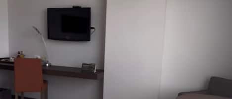 A hotel room with a bed, a desk, a chair, a television, and a small table.
