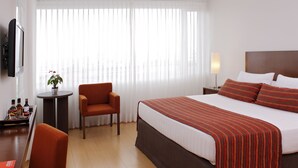 A hotel room with a bed, a desk, a chair, a TV, and a window with curtains. - Hotel Estelar El Cable (Manizales)