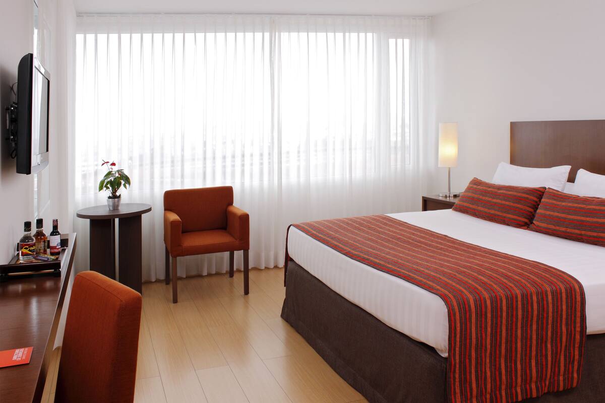 Ein Hotelzimmer mit Bett, Schreibtisch, Stuhl, Fernseher und einem Fenster mit Vorhängen.