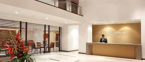 A modern hotel lobby with a reception desk, seating area, and a decorative plant.
