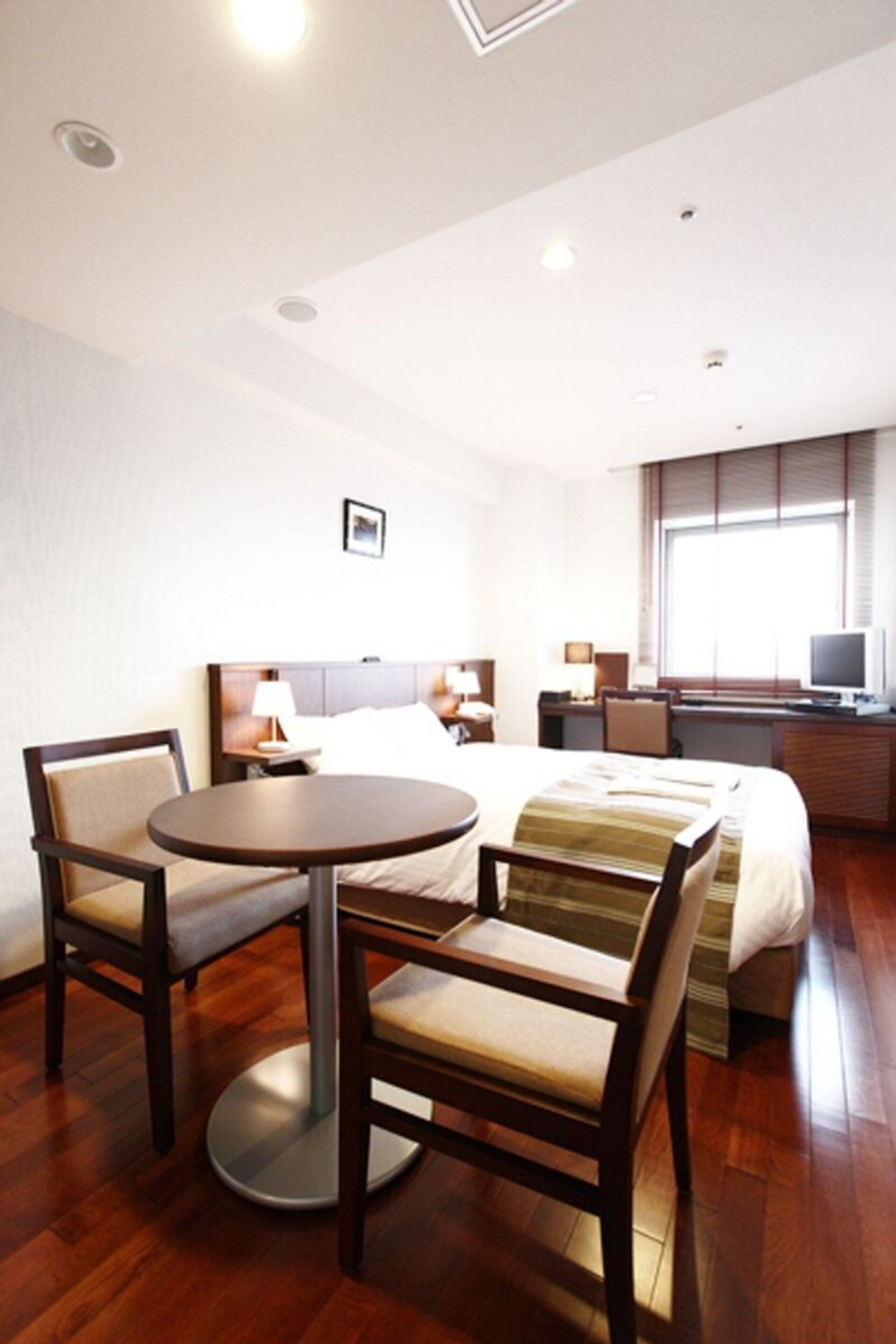 Ein Hotelzimmer mit Bett, Schreibtisch, Stuhl, rundem Tisch und Fernseher.