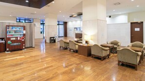 A spacious lobby with wooden flooring, a vending machine, and several seating areas with tables and chairs. - Sutton Hotel Hakata City (Fukuoka)