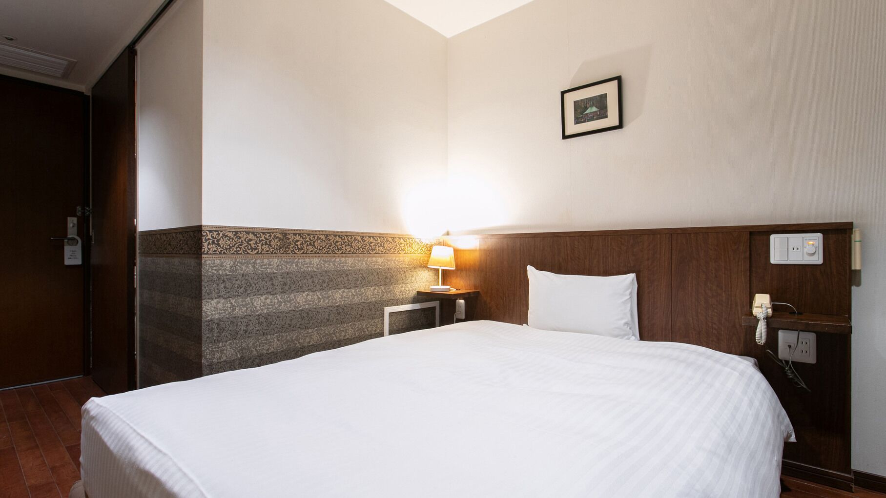 Quarto de hotel com uma cama grande, mesa de cabeceira com abajur, telefone e quadro na parede.