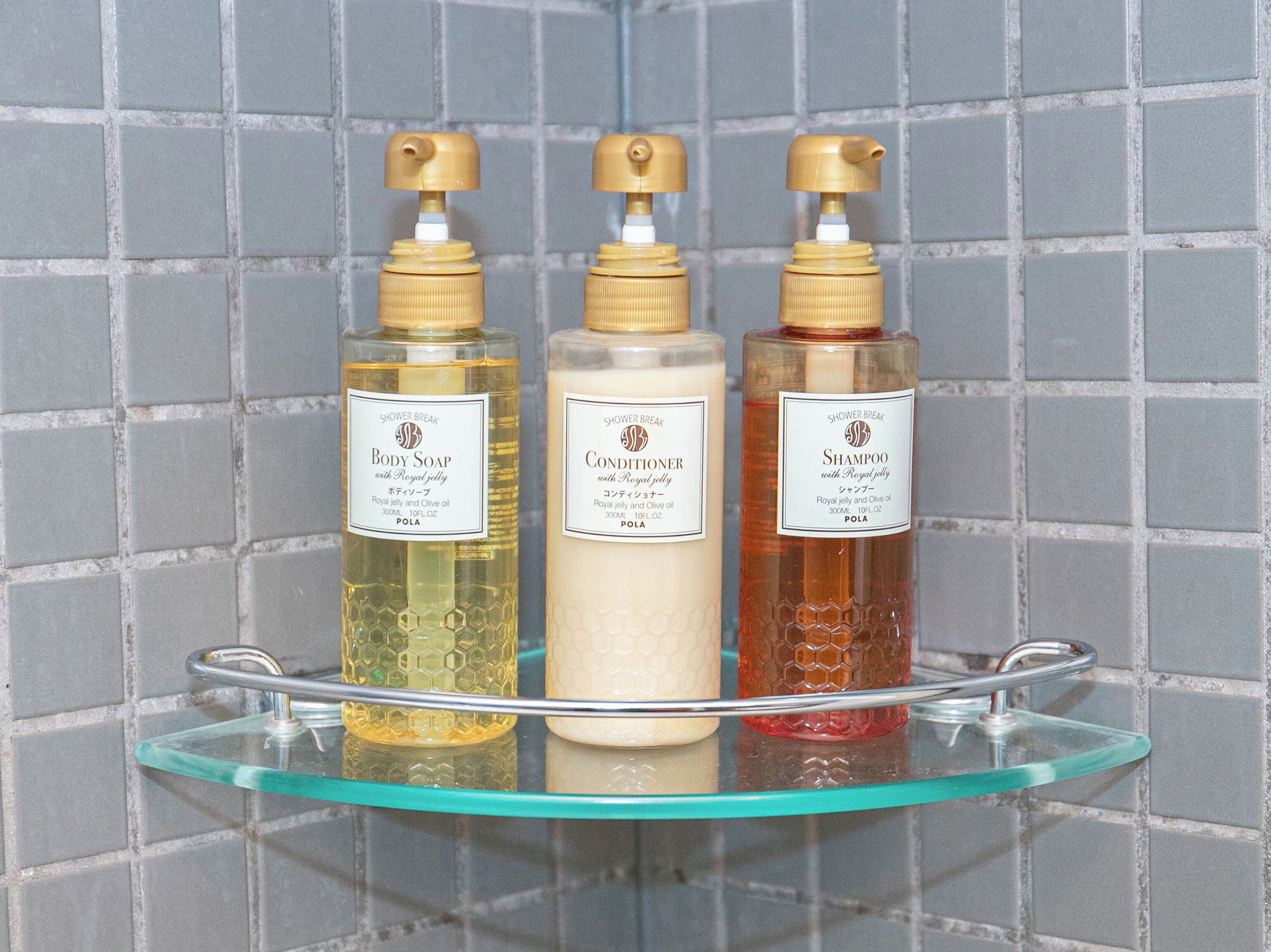 Three bottles of shower products on a glass shelf against a tiled wall.