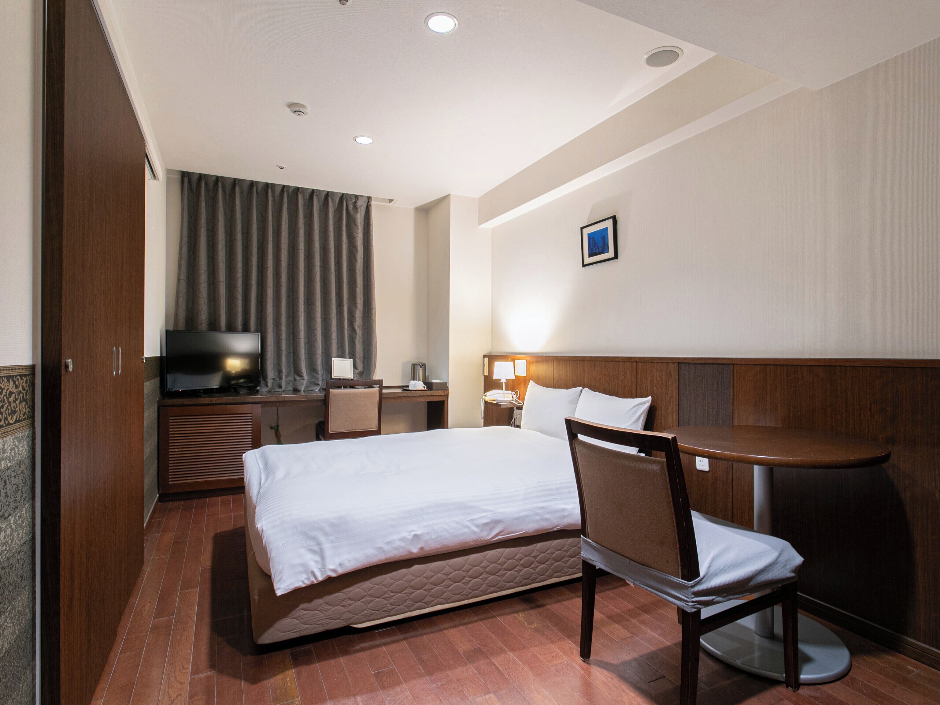 A hotel room with a bed, a desk, a chair, a television, and a window with curtains.