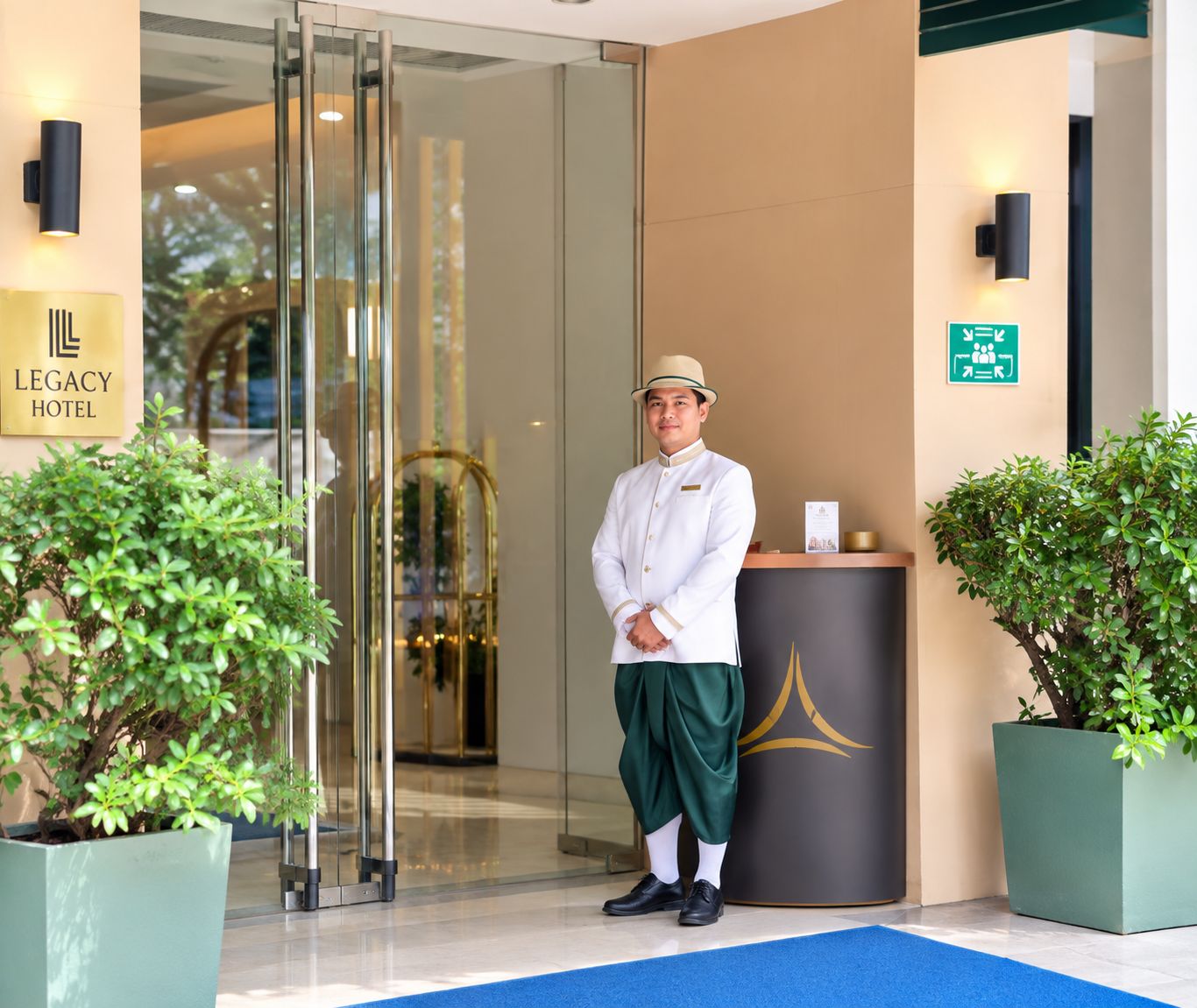 Een hotel ingang met een receptiebalie, een glazen deur en een blauw tapijt dat naar binnen leidt.