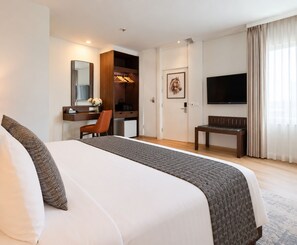 A hotel room with a large bed, a desk with a chair, a television, and a door with a horse painting.