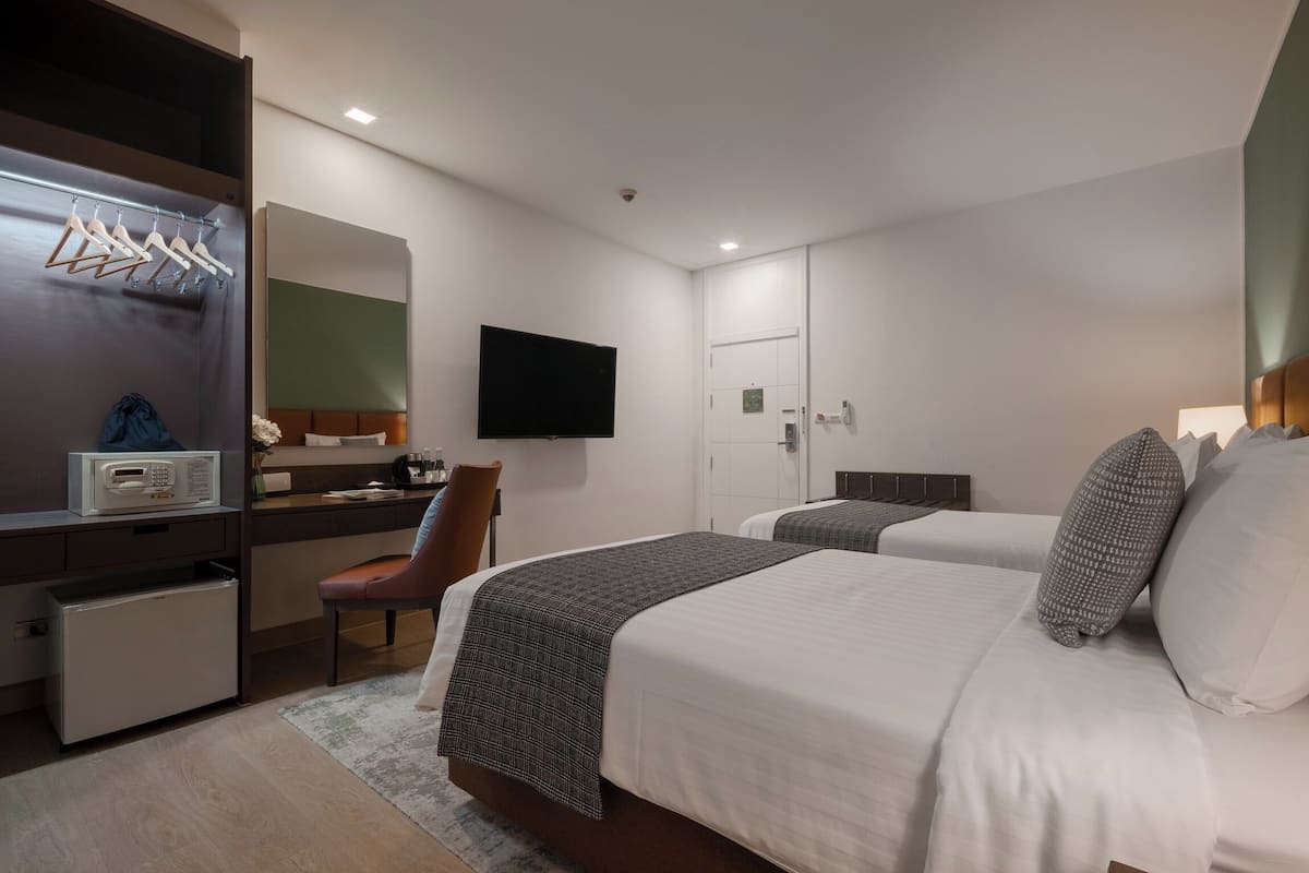 A hotel room with two beds, a desk with a computer, a TV, and a wardrobe.
