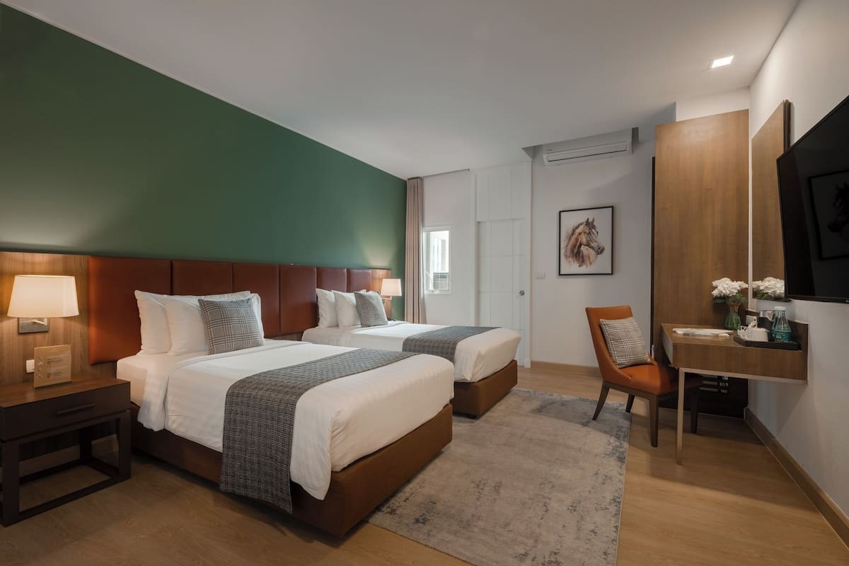 A hotel room with two beds, a desk, a chair, a TV, and a framed picture on the wall.