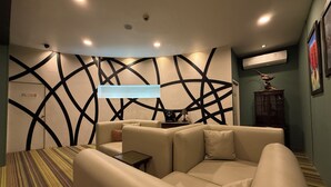 A modern living room with a sofa, a patterned rug, a wall with geometric designs, and recessed ceiling lighting. - The Legacy Hotel Nana Sukhumvit, Aspira Collection (Bangkok)