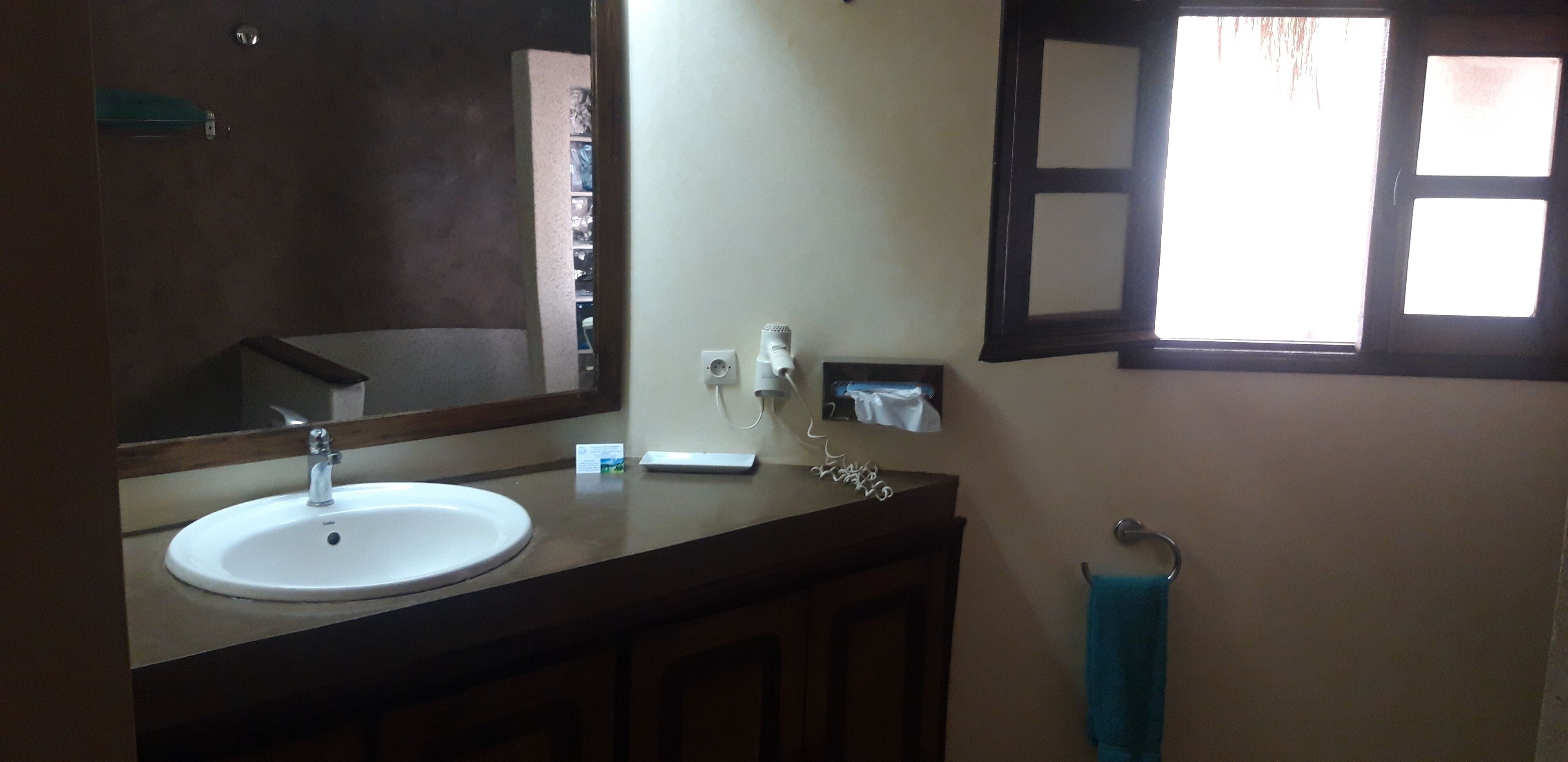 A bathroom with a white sink, a mirror, a towel rack, and a window with blinds.