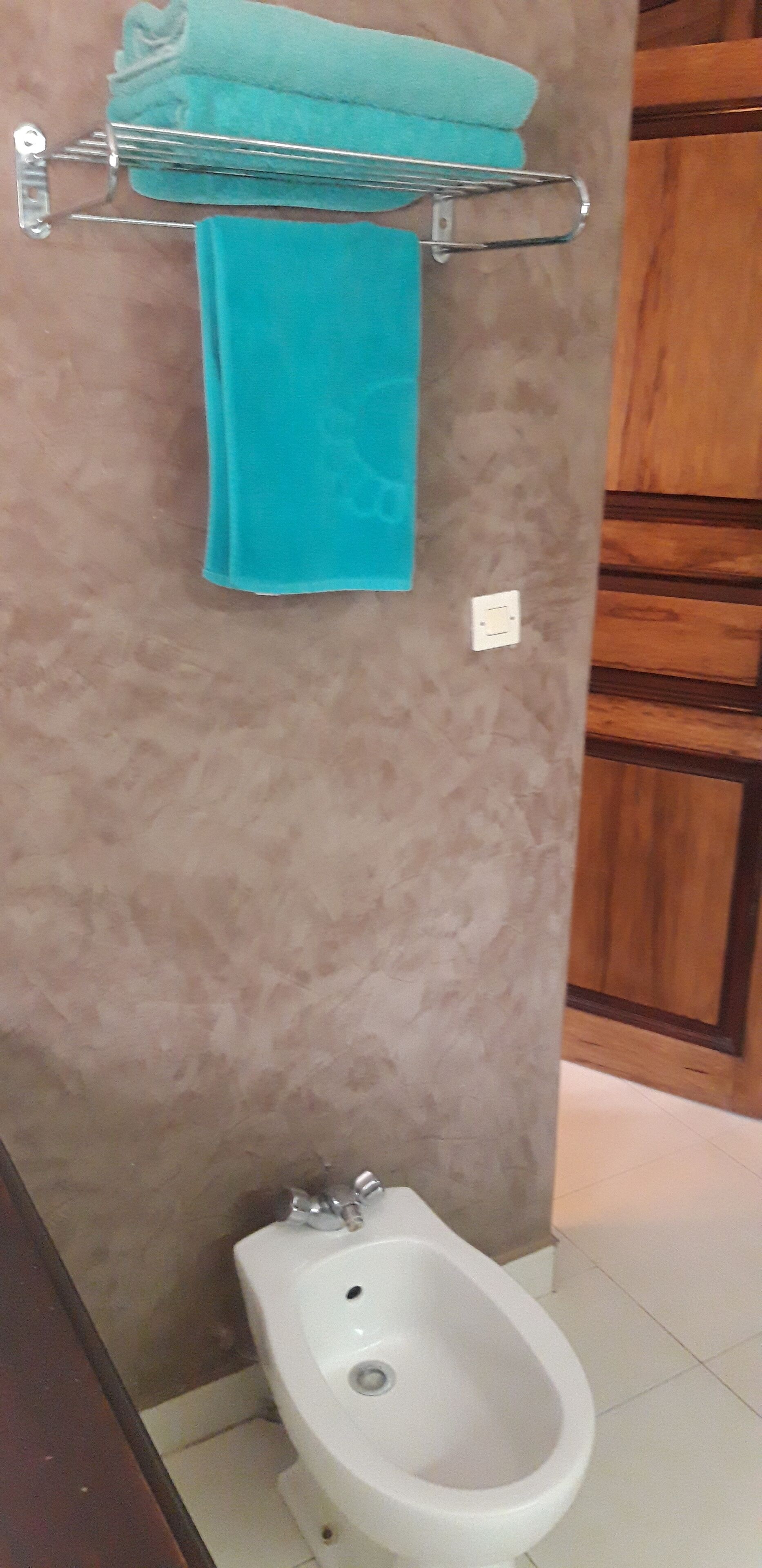 A bathroom with a bidet, a towel rack with a blue towel, and wooden cabinets.