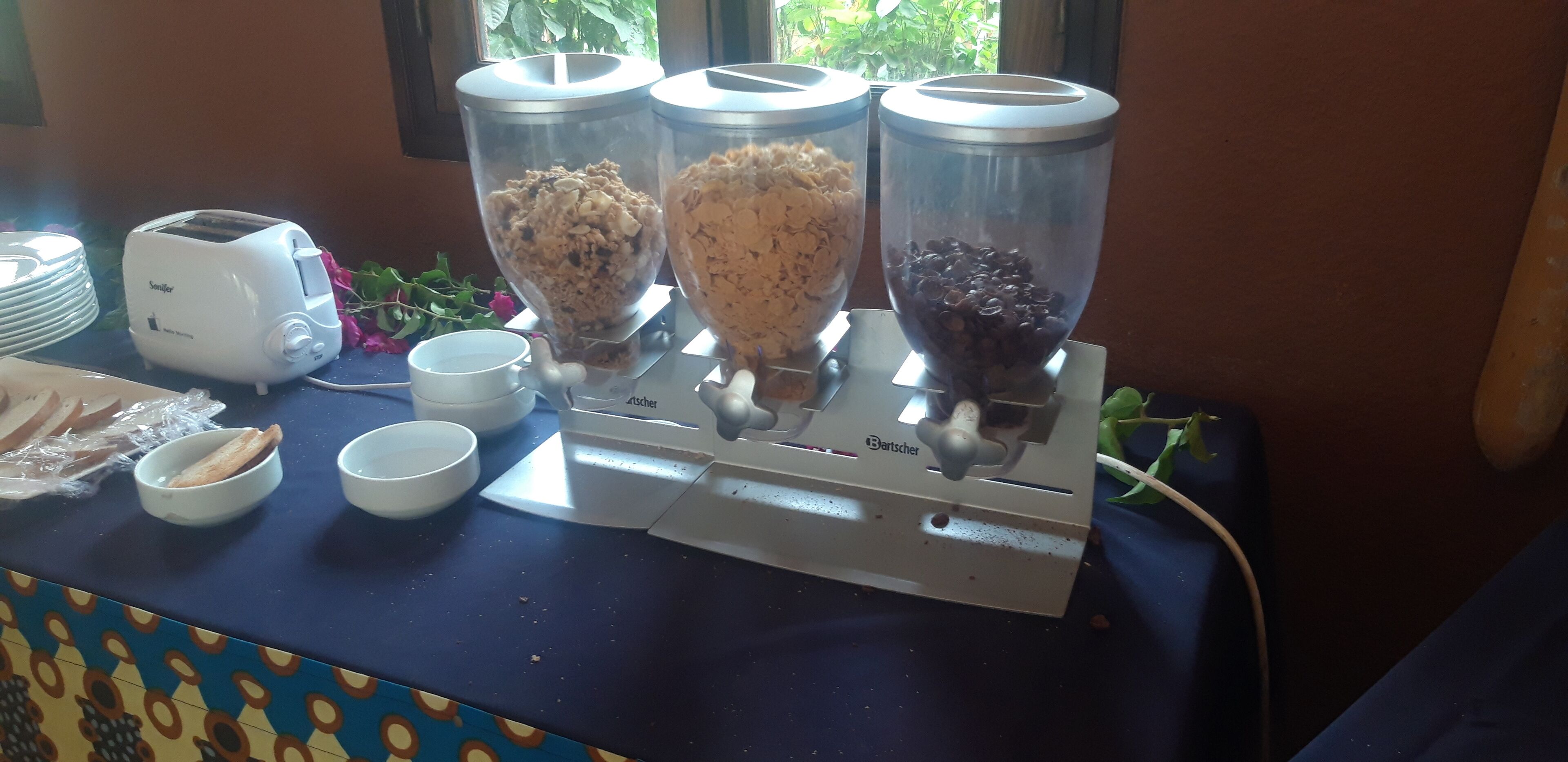 A buffet setup with a toaster, three food dispensers, and several bowls.
