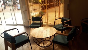 Un coin salon avec une table ronde en bois et quatre chaises, une porte vitrée donnant sur l’extérieur et une vue sur la rue à travers cette porte.
