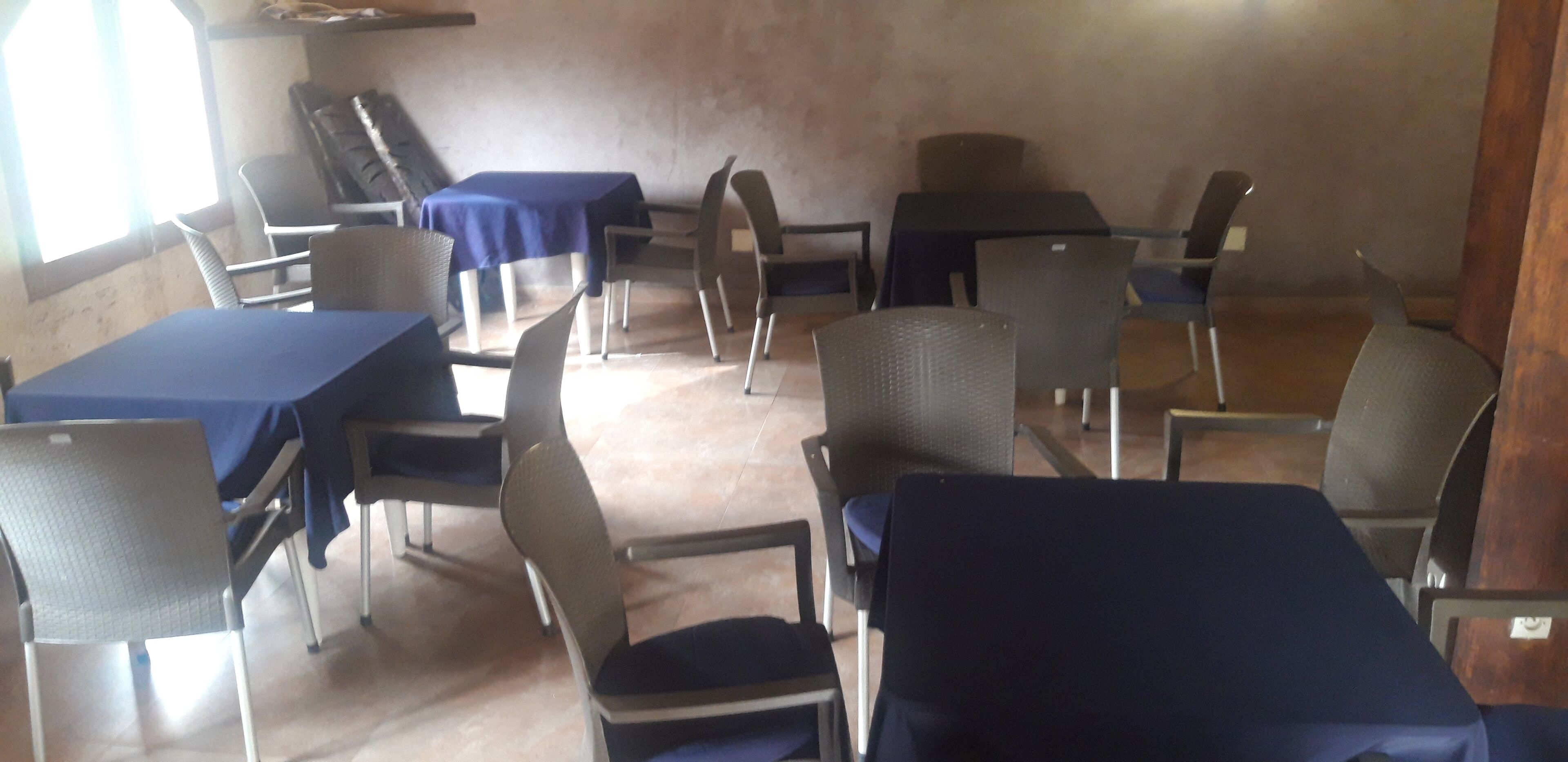 A room with several tables and chairs, some covered with blue tablecloths.