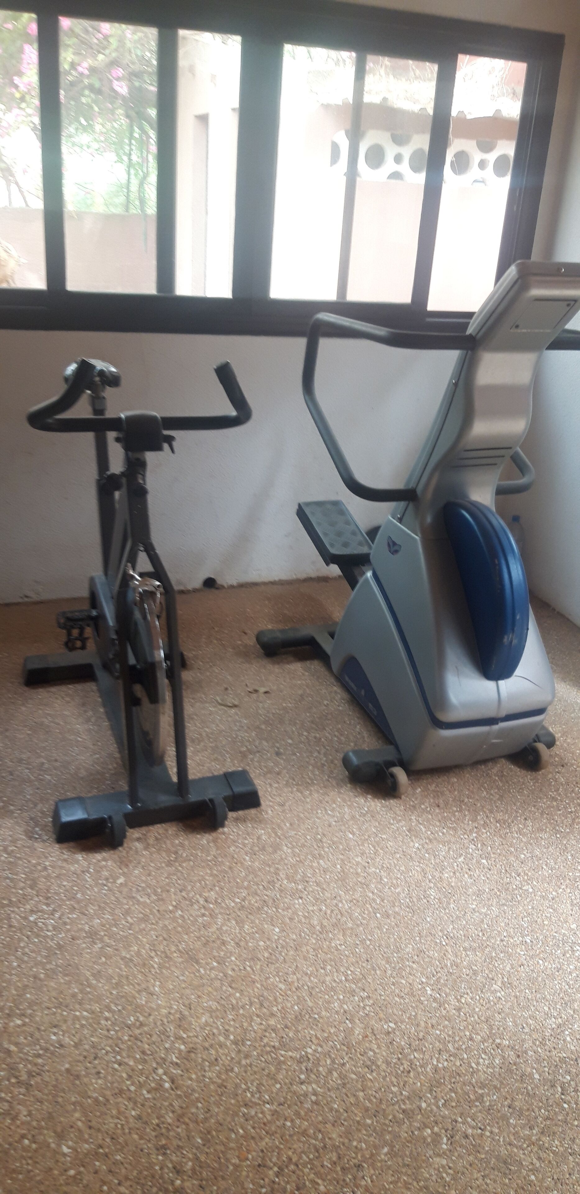 Two stationary bikes in a room with a window and a textured floor.