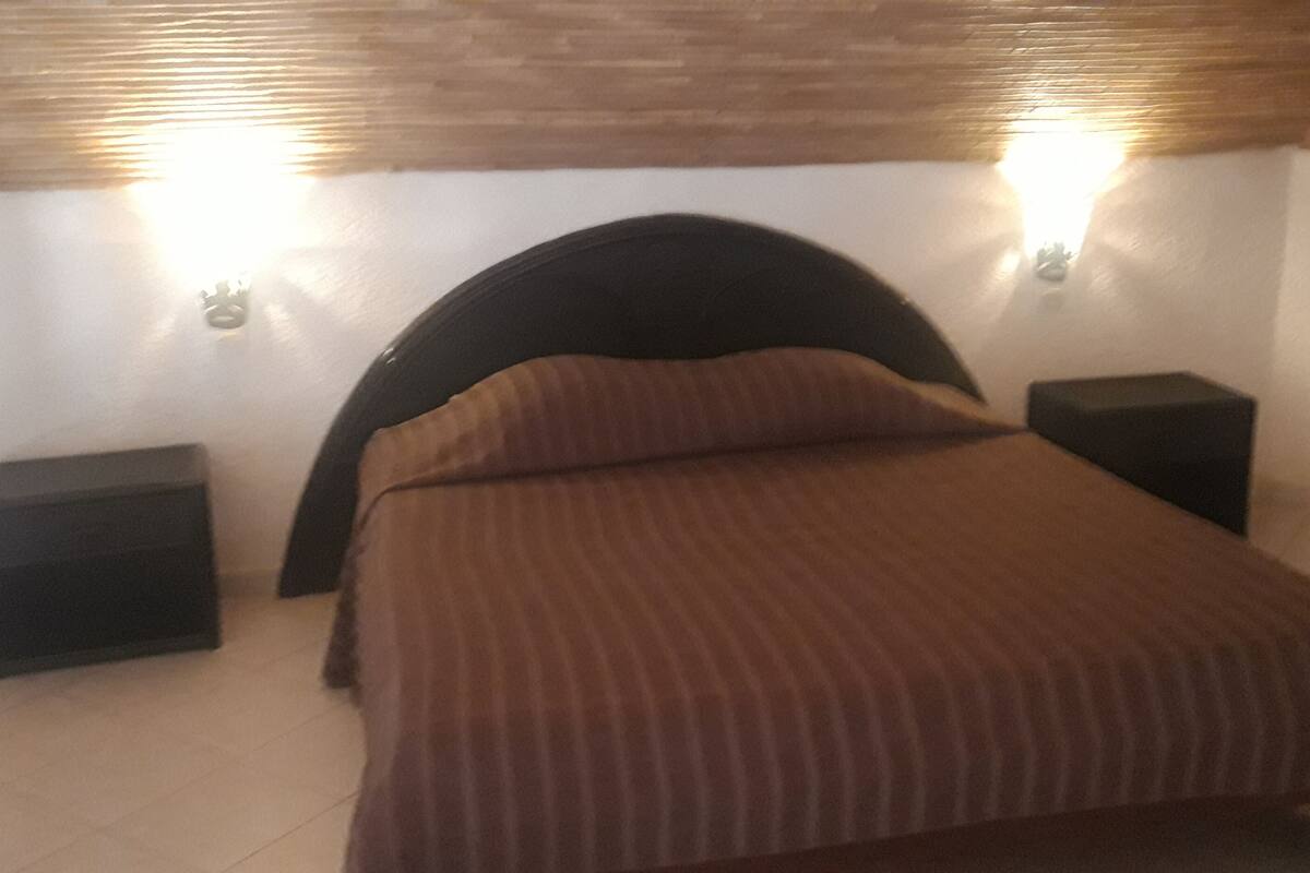 Quarto com uma cama, duas mesas de cabeceira e luminárias fixadas na parede.