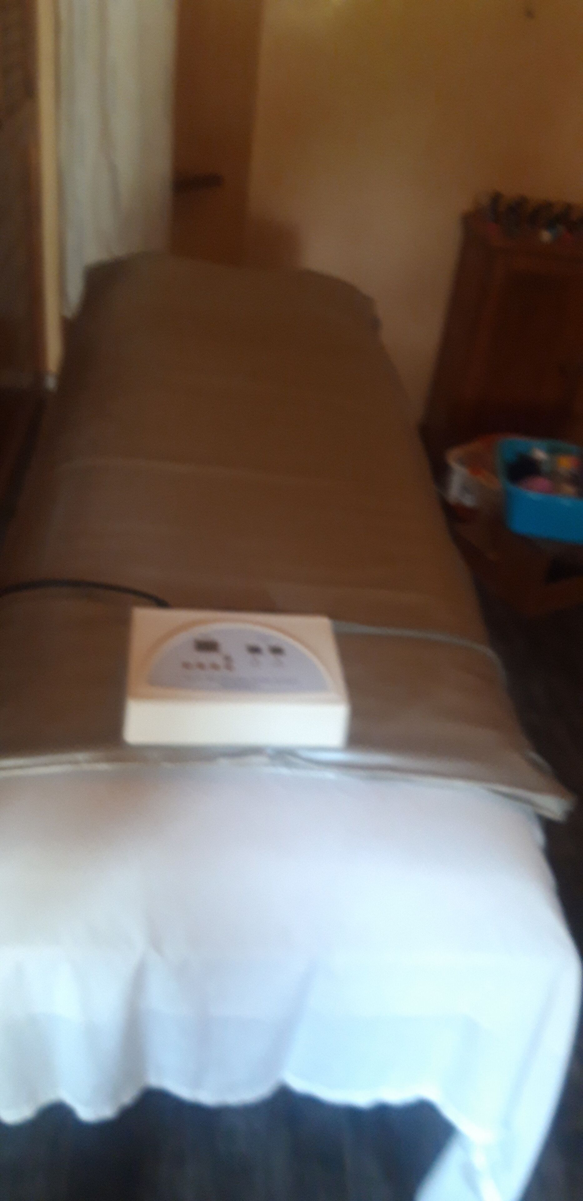 A bed with a white mattress and a white blanket. There is a small white device on the bed.