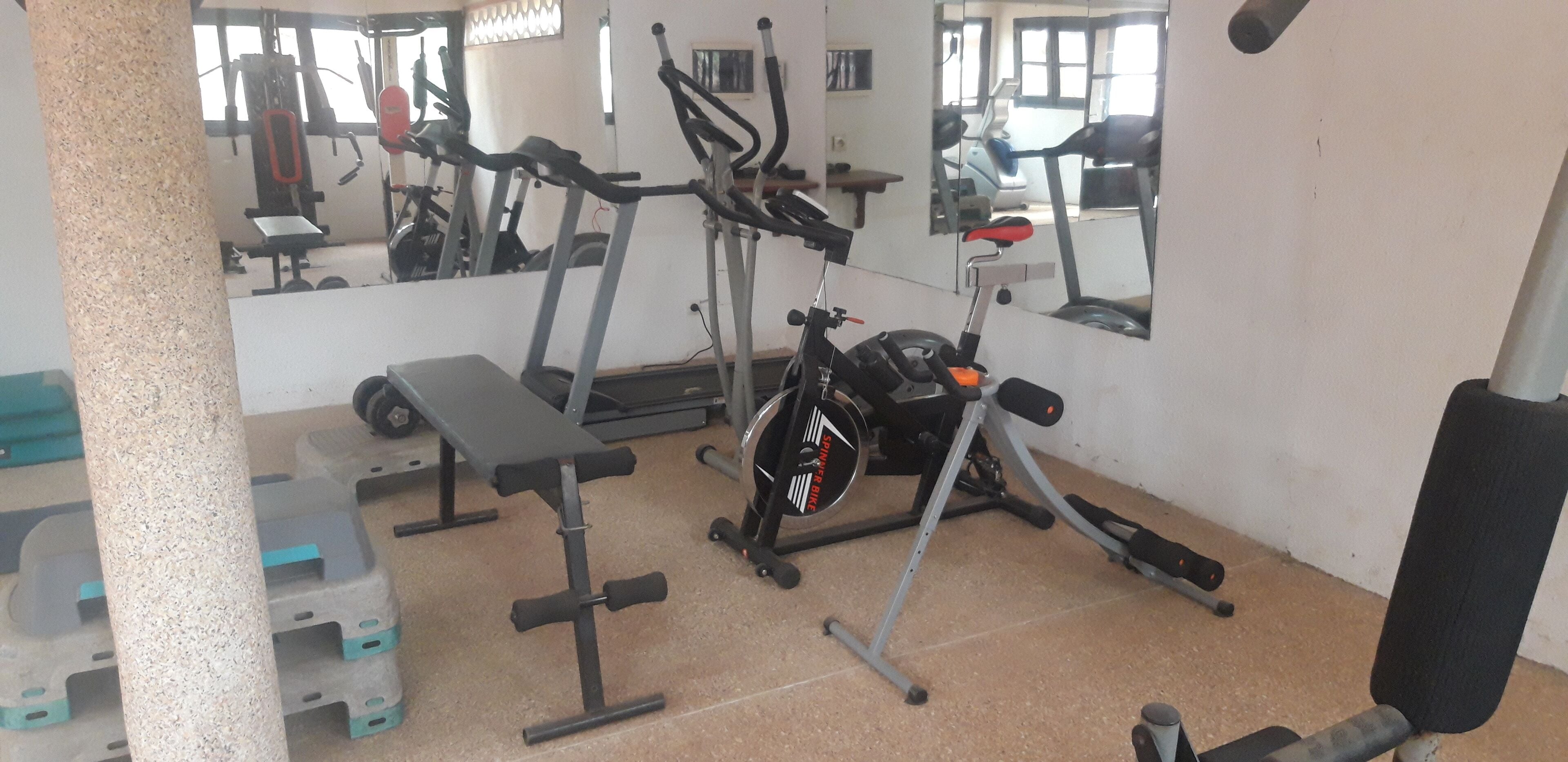 Un gimnasio con equipo de ejercicio, incluyendo cintas de correr, una bicicleta estática y bancos de pesas.