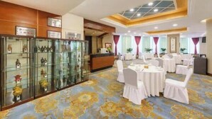 A banquet hall with round tables and white chairs, a reception area, and a glass display case with decorative items. - Lee Wan Hotel (Dalian)