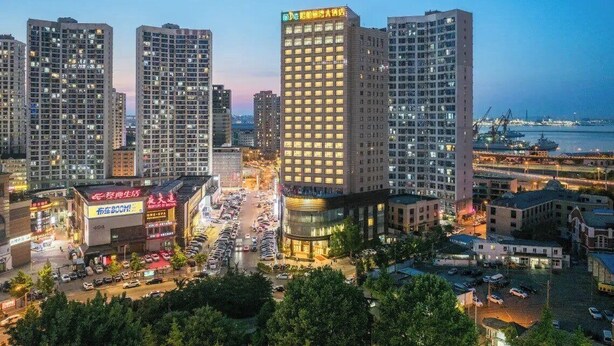 A high-rise building with multiple floors, surrounded by other buildings and a busy street with cars. - Lee Wan Hotel (Dalian)