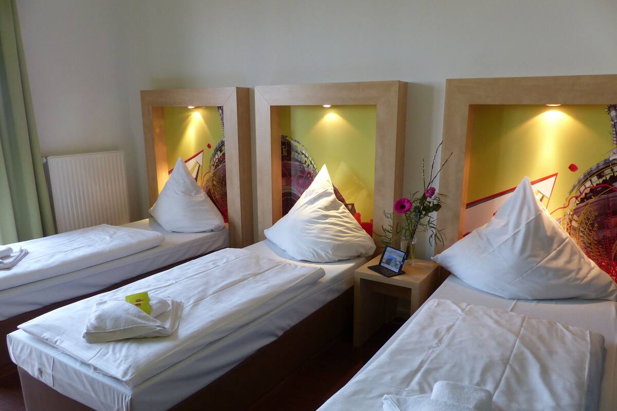 Une chambre d’hôtel avec deux lits simples, chacun agrémenté de draps et d’oreillers blancs, une petite table de chevet avec un ordinateur portable et un vase rempli de fleurs.